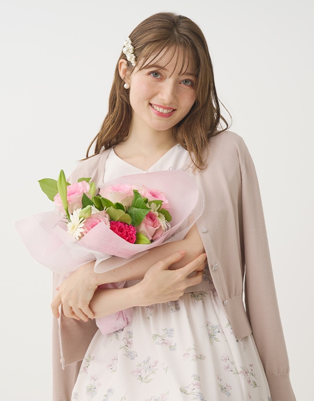 アイボリーの花柄のワンピースと、グレイッシュピンクのカーディガンを身に着けた女性