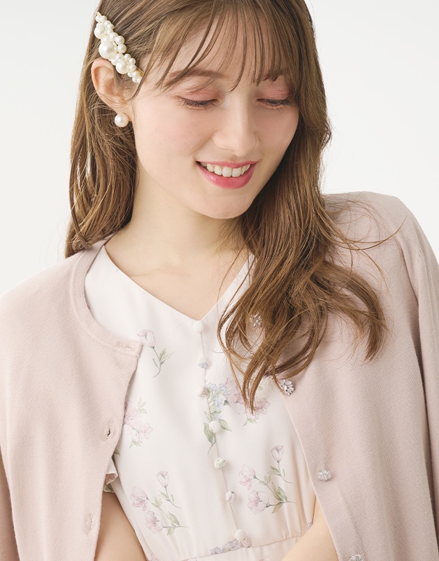 アイボリーの花柄のワンピースと、グレイッシュピンクのカーディガンを身に着けた女性