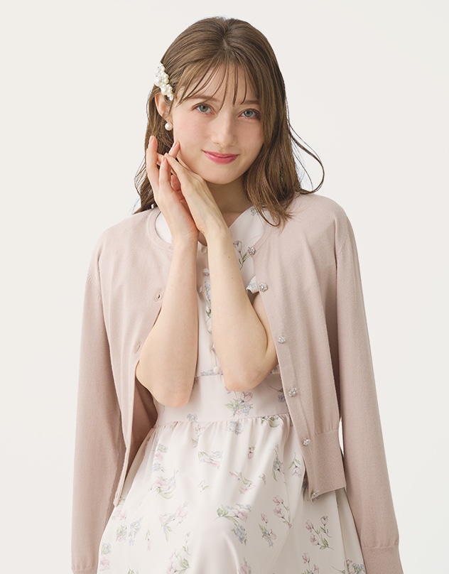 アイボリーの花柄のワンピースと、グレイッシュピンクのカーディガンを身に着けた女性