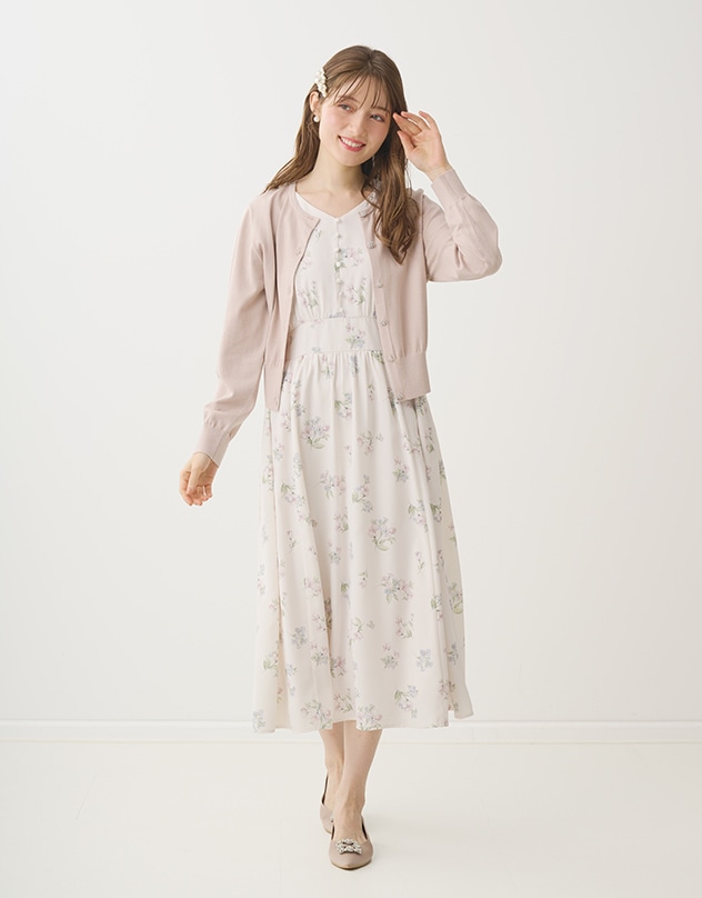 アイボリーの花柄のワンピースと、グレイッシュピンクのカーディガンを身に着けた女性