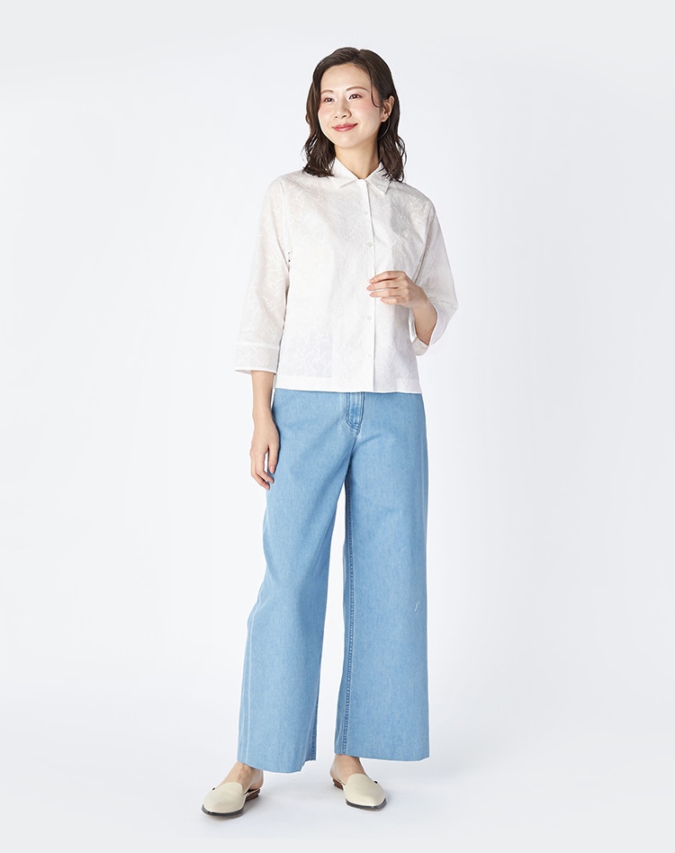 ホワイト地にホワイトの花柄刺繍のシャツとデニムパンツを身に着けた女性