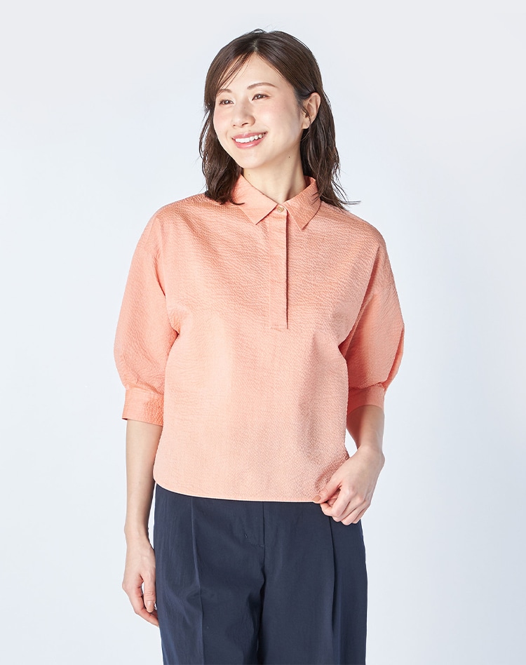 ピンクのブラウスとネイビーのパンツを身に着けた女性