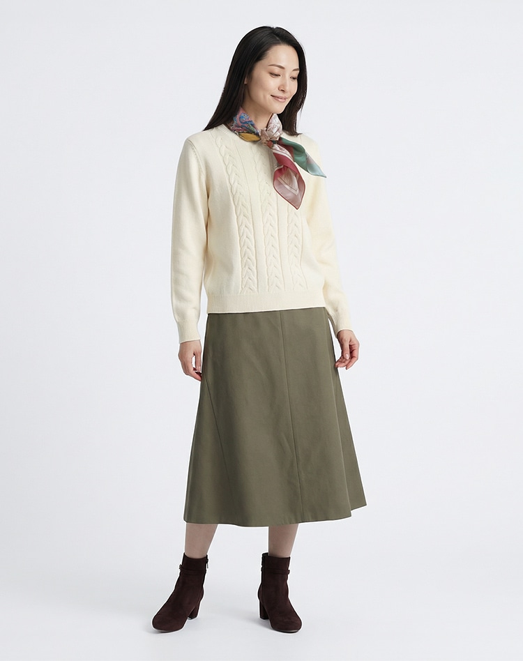 ホワイトのニットとダークグリーンのスカートを身に着けた女性