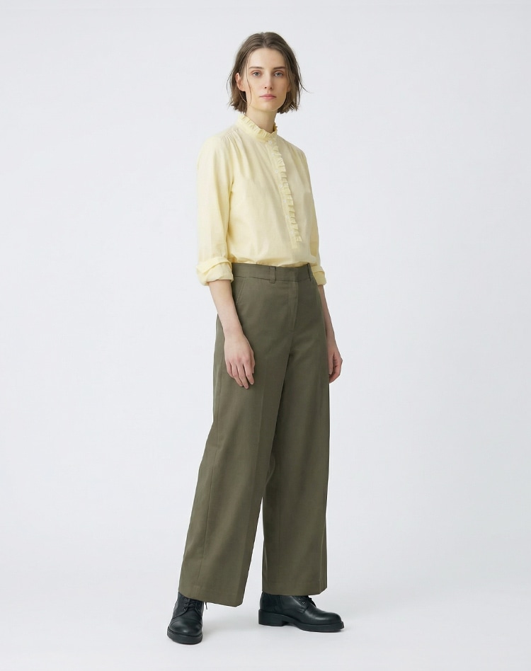 イエローのブラウスとダークグリーンのチノパンツを身に着けた女性