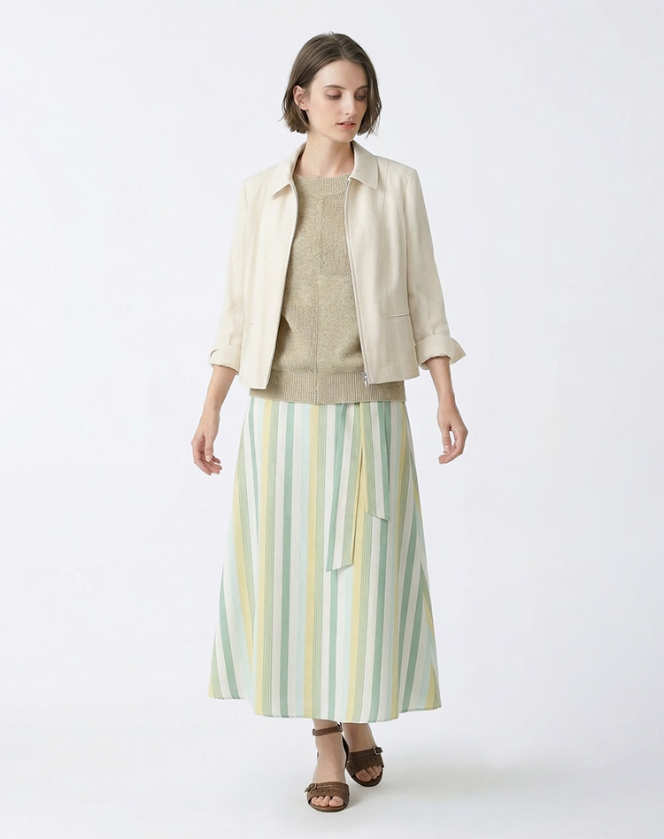 ホワイトのジャケット、ベージュのニット、グリーンのストライプのスカートを身に着けた女性