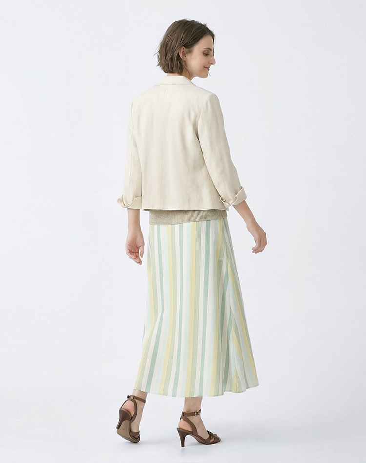 ホワイトのジャケット、ベージュのニット、グリーンのストライプのスカートを身に着けた女性