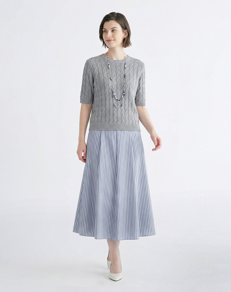 グレーのニット、ブルーのストライプのスカートを身に着けた女性