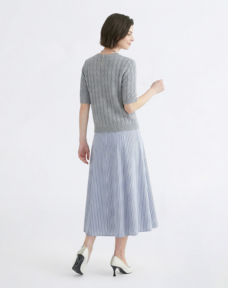 グレーのニット、ブルーのストライプのスカートを身に着けた女性