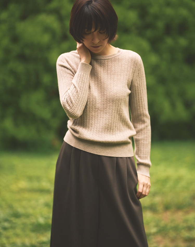 ベージュのニット、ダークブラウンのパンツを身に着けた女性