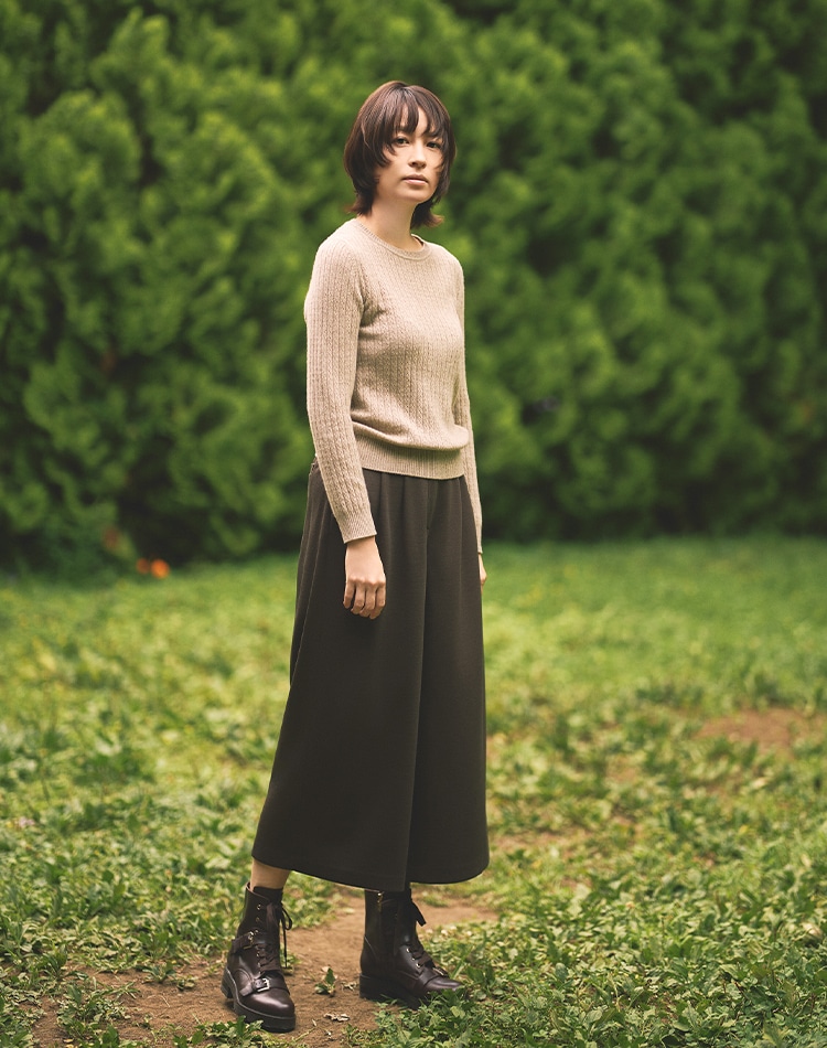 ベージュのニット、ダークブラウンのパンツを身に着けた女性