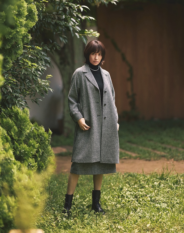 グレーのコート、ブラックのニット、グレーのスカートを身に着けた女性