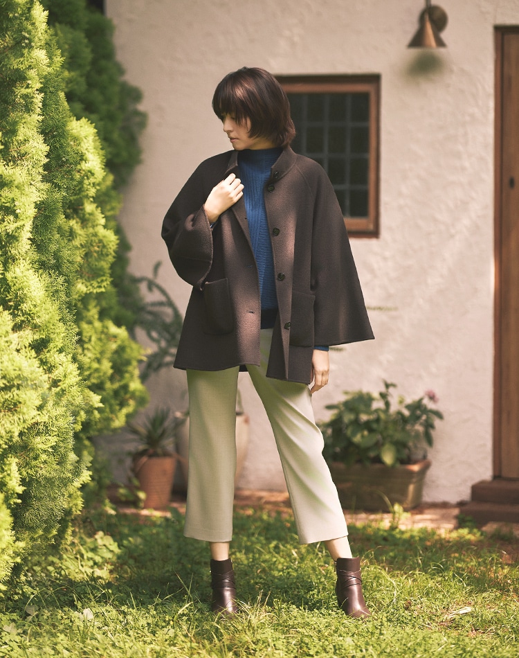 ダークブラウンのコート、ブルーのニット、グレーのパンツを身に着けた女性