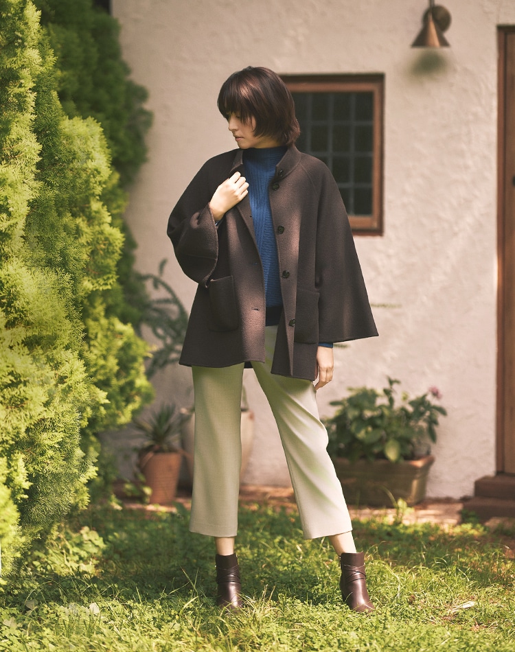 ダークブラウンのコート、ブルーのニット、グレーのパンツを身に着けた女性
