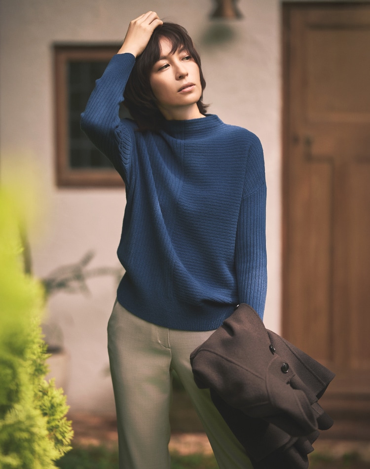 ブルーのニット、グレーのパンツを身に着けた女性