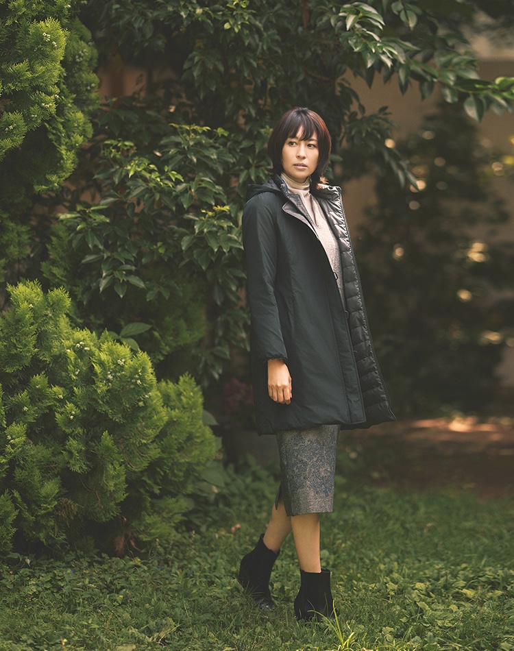 ブラックのダウンコート、グレーのワンピース、ホワイトのカットソーを身に着けた女性