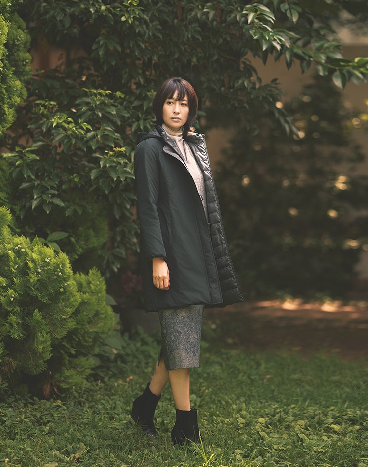 ブラックのダウンコート、グレーのワンピース、ホワイトのカットソーを身に着けた女性