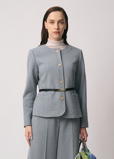 グレーのジャケット、ベージュのタートルネックニット、グレーのパンツを身に着けた女性