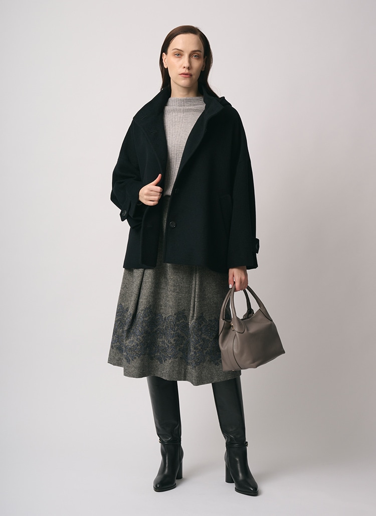 ブラックのショートコート、グレー のニット、グレー のエンブロイダリー柄のスカートを身に着けた女性