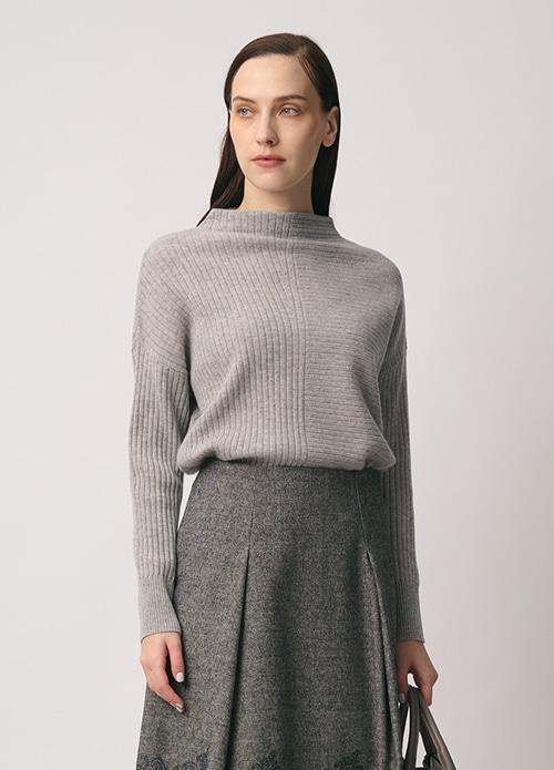 グレー のニット、グレー のエンブロイダリー柄のスカートを身に着けた女性