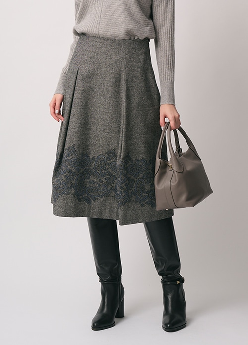 グレー のニット、グレー のエンブロイダリー柄のスカートを身に着けた女性