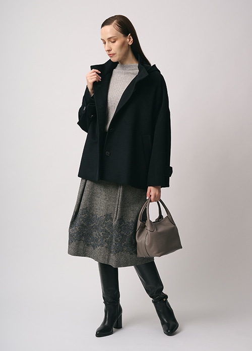 ブラックのショートコート、グレー のニット、グレー のエンブロイダリー柄のスカートを身に着けた女性