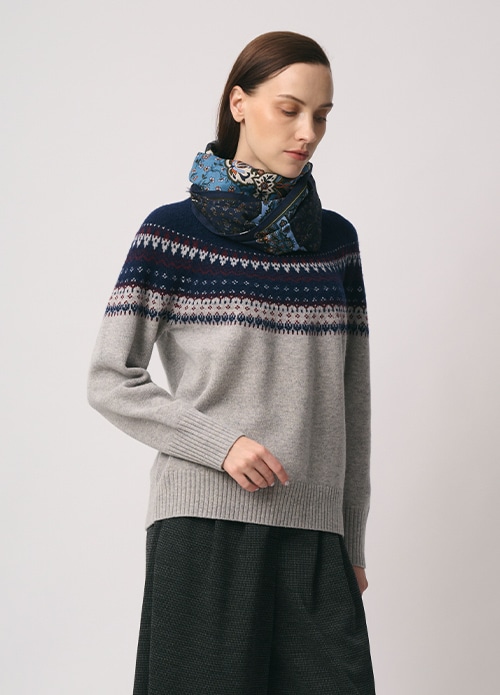 ブルーのスカーフ、グレーのフェアアイル柄のニット、チャコールグレーのパンツを身に着けた女性