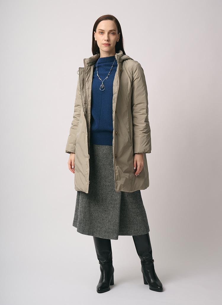 ベージュのダウンコート、ブルーのニット、グレーのスカートを身に着けた女性