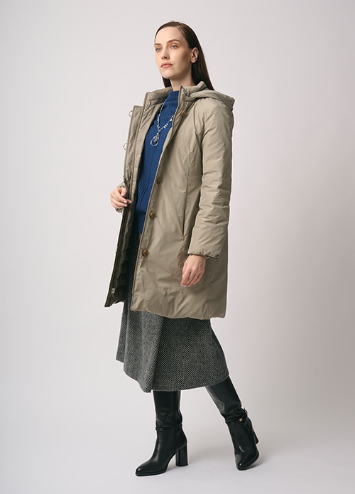 ベージュのダウンコート、ブルーのニット、グレーのスカートを身に着けた女性