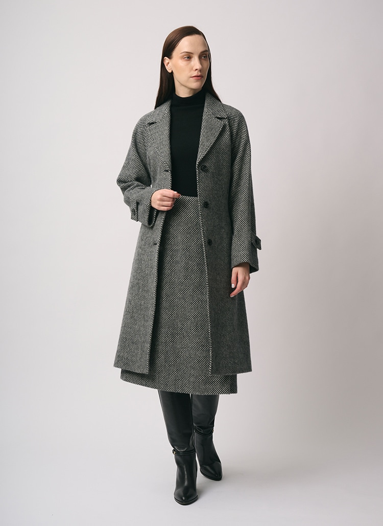 グレーのコート、ブラックのニット、グレーのスカートを身に着けた女性