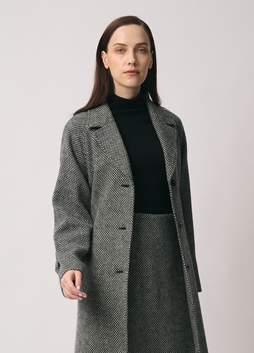 グレーのコート、ブラックのニット、グレーのスカートを身に着けた女性