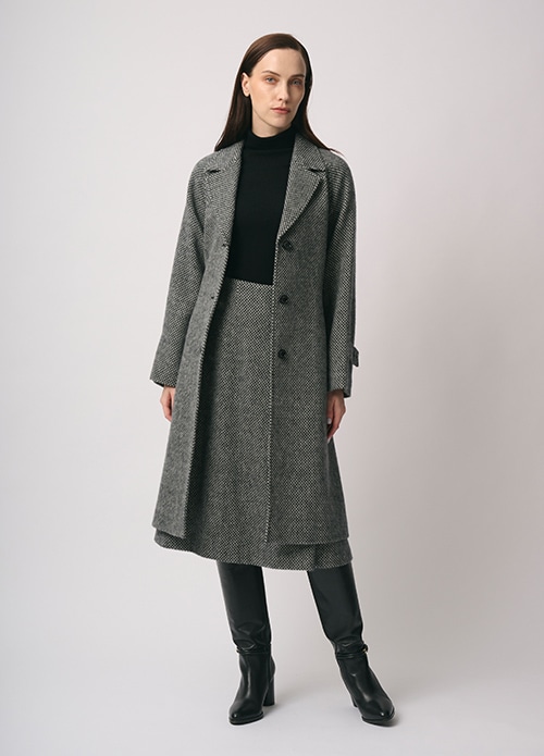 グレーのコート、ブラックのニット、グレーのスカートを身に着けた女性