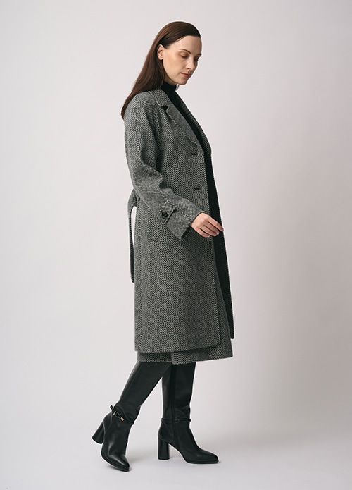 グレーのコート、ブラックのニット、グレーのスカートを身に着けた女性