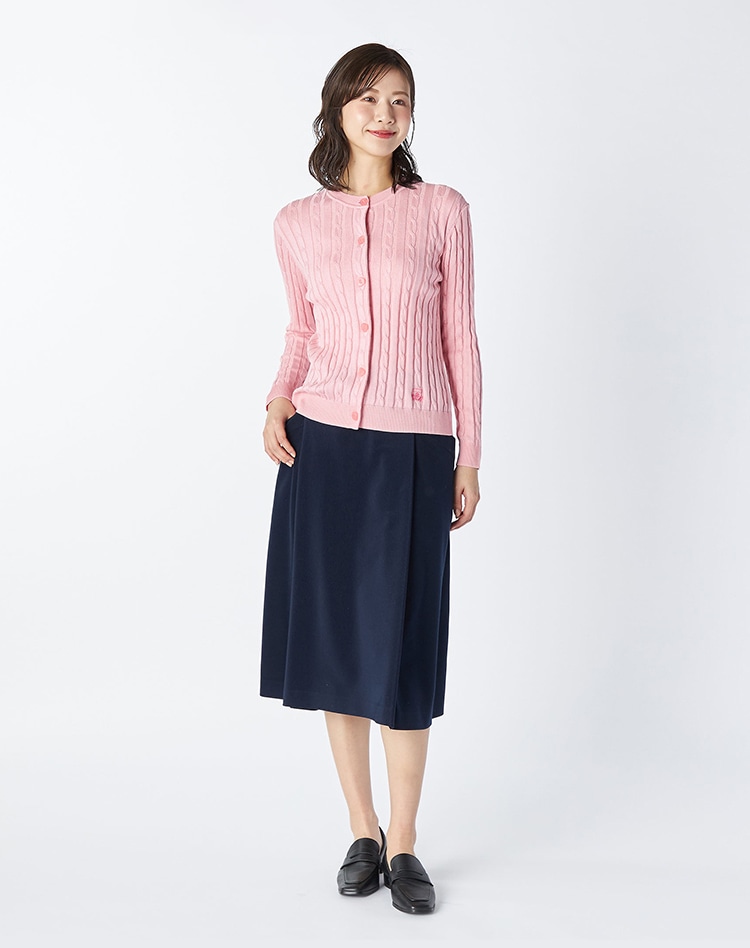 ピンクのカーディガンとネイビーのスカートを身に着けた女性