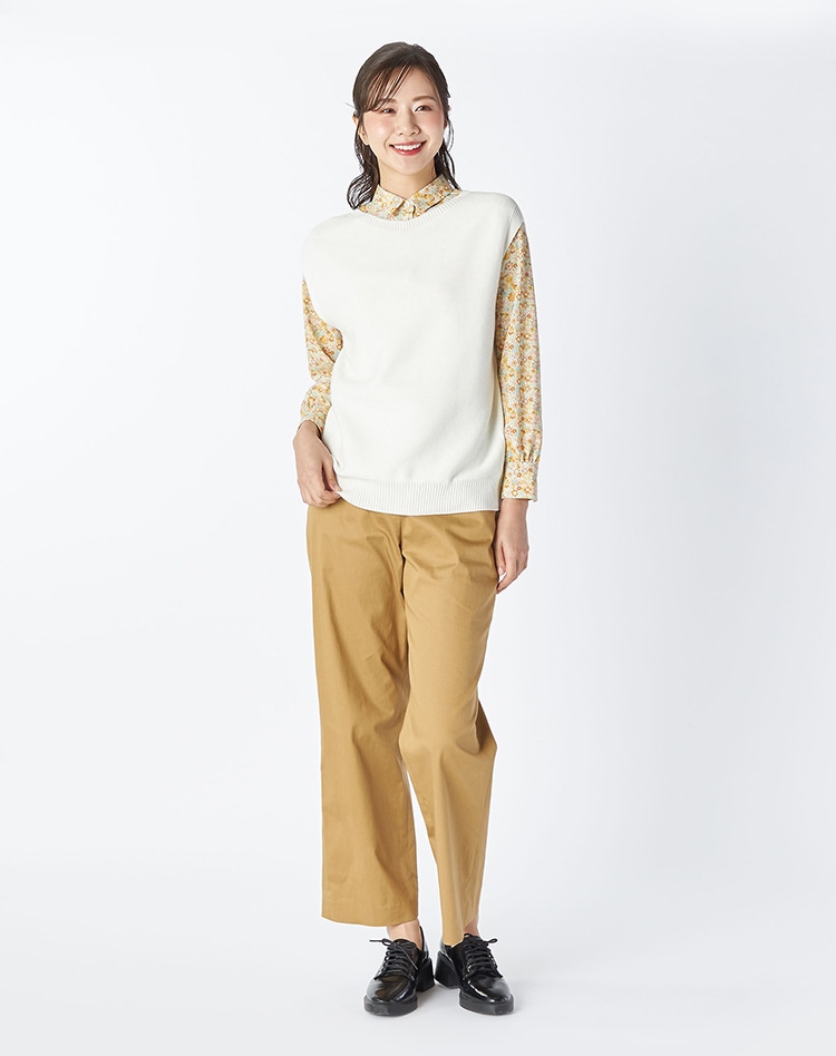 ホワイトのニットとイエローの花柄のブラウス、ブラウンのパンツを身に着けた女性
