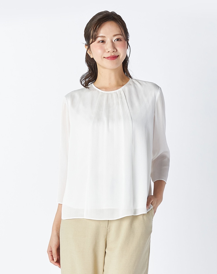 ホワイトのブラウスとベージュのセットアップパンツを身に着けた女性