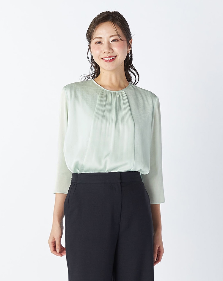 ライトグリーンのブラウスとブラックのセットアップパンツを身に着けた女性