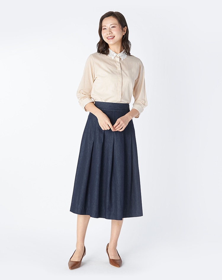 ベージュのストライプブラウスとネイビーのスカートを身に着けた女性
