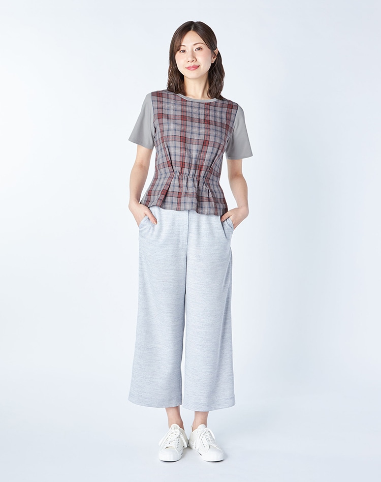 グレーのチェック柄のプルオーバーとライトブルーのパンツを身に着けた女性