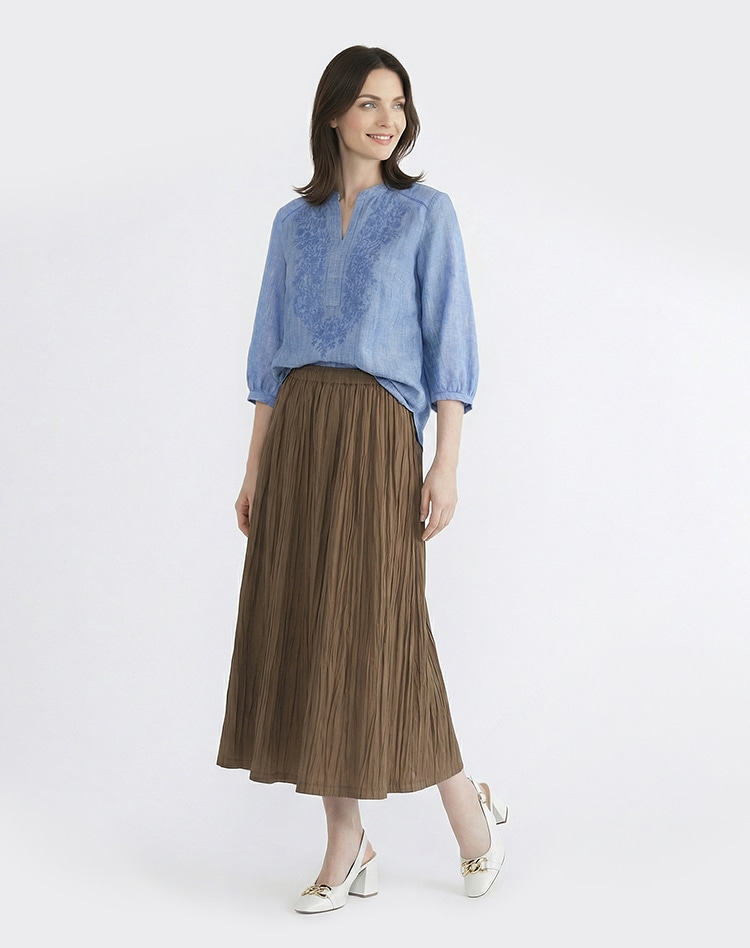ライトブルーの五分袖ブラウスとブラウンのスカートを身に着けた女性