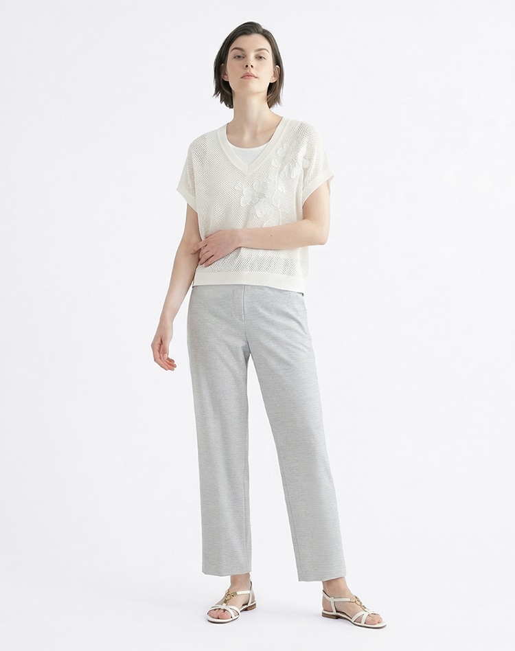 ホワイトのニットとグレーのワイドパンツを身に着けた女性