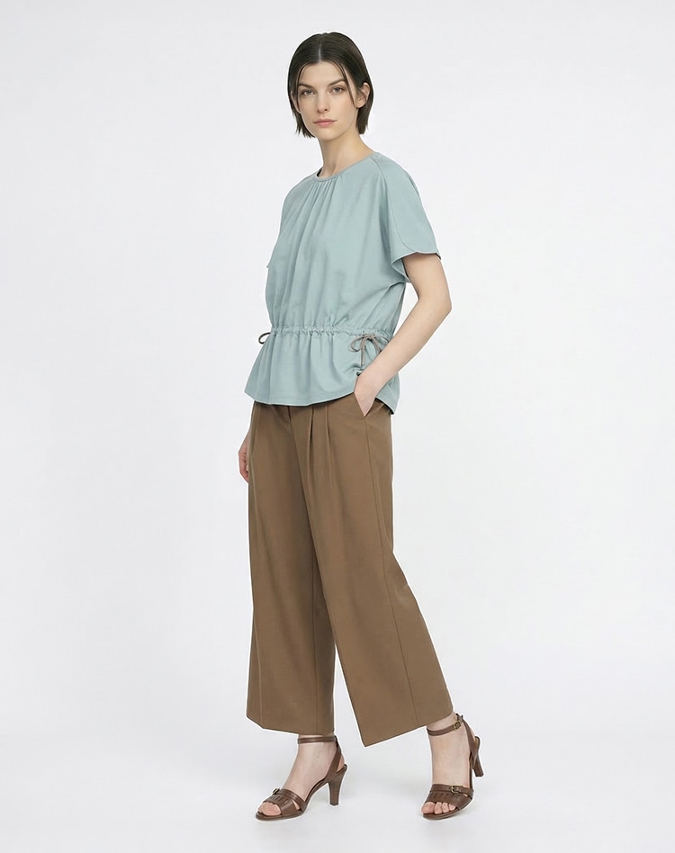 ライトグリーンのカットソーとブラウンのパンツを身に着けた女性