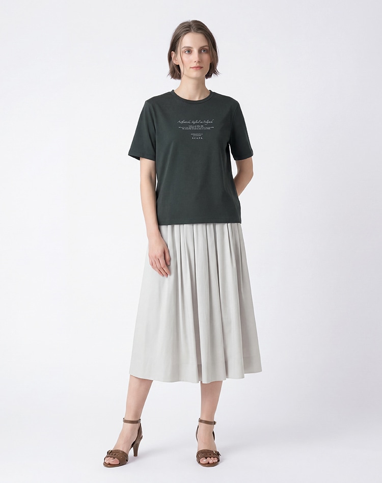 モスグリーンのカットソーとライトグレーのスカートを身に着けた女性