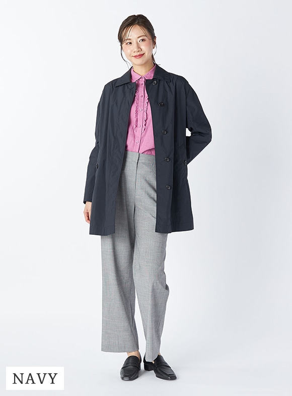 ネイビーのコートとパープルのブラウスとグレーのパンツを身に着けた女性