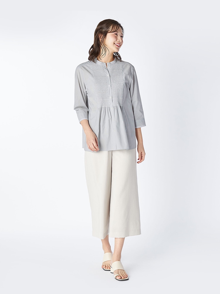 グレーのブラウスとオフホワイトのパンツを着た女性