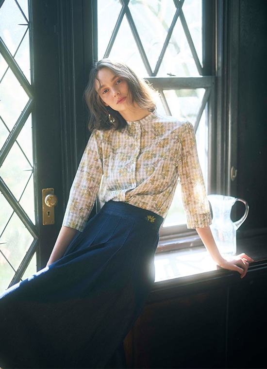 ミモザ柄のブラウスとミモザのワンポイント柄が入ったデニムスカートを履いている女性