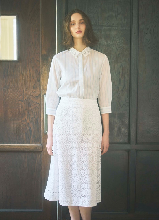 ストライプ柄の白ブラウスとレース柄の白いロングスカートを履いた女性