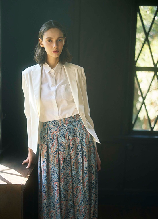 白ジャケットと白ブラウスとペイズリー柄のロングスカートを履いた女性