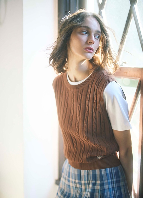 白いTシャツとブラウンベストと青いチェック柄のスカートを履いた女性