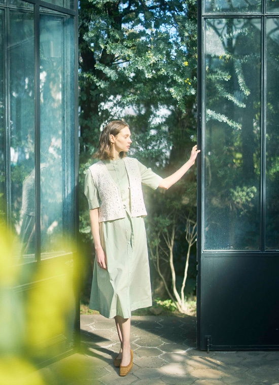 淡いグリーンのワンピースと白いベストを着た女性